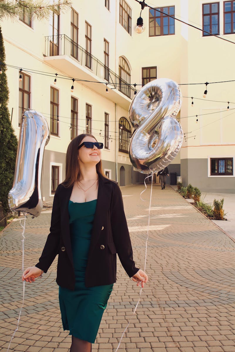 A young woman celebrates her 18th birthday with silver balloons outdoors.