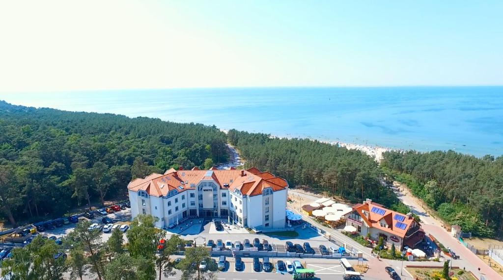 Widok na nadmorski hotel otoczony lasem, z plażą w tle. Miejsce idealne na wakacje, z parkingiem i innymi obiektami usługowymi.